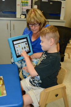 Young male student working on a tablet device with female teacher - private special education school at NJEDDA