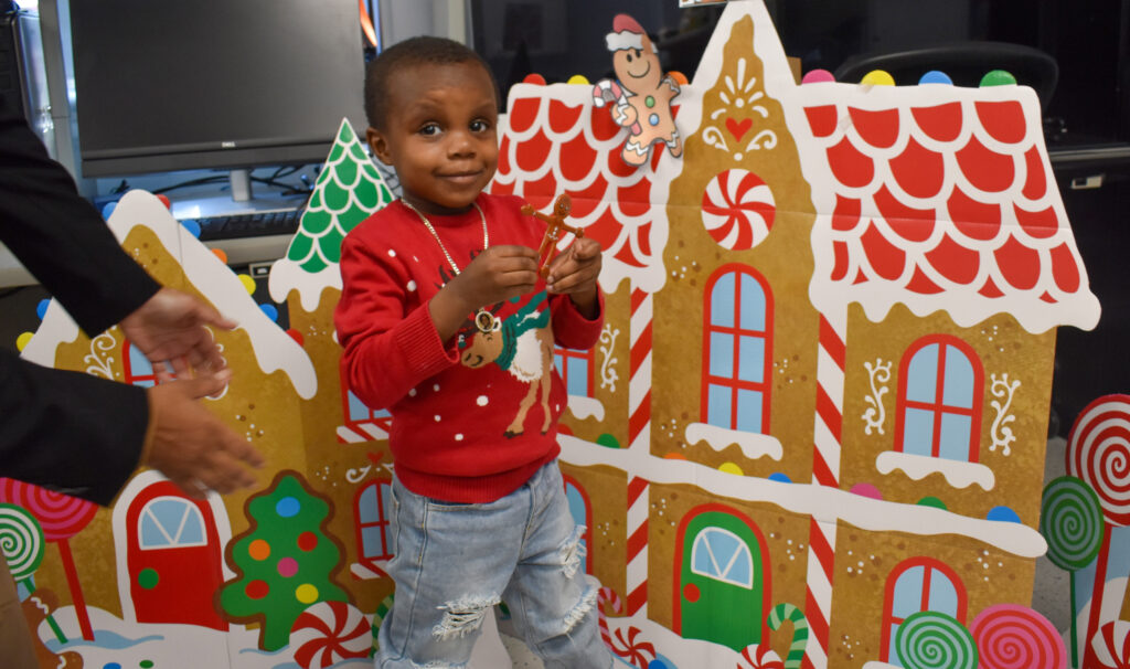 African American male preschool student playing in holiday themed setting and standing in front of a giant gingerbread house
