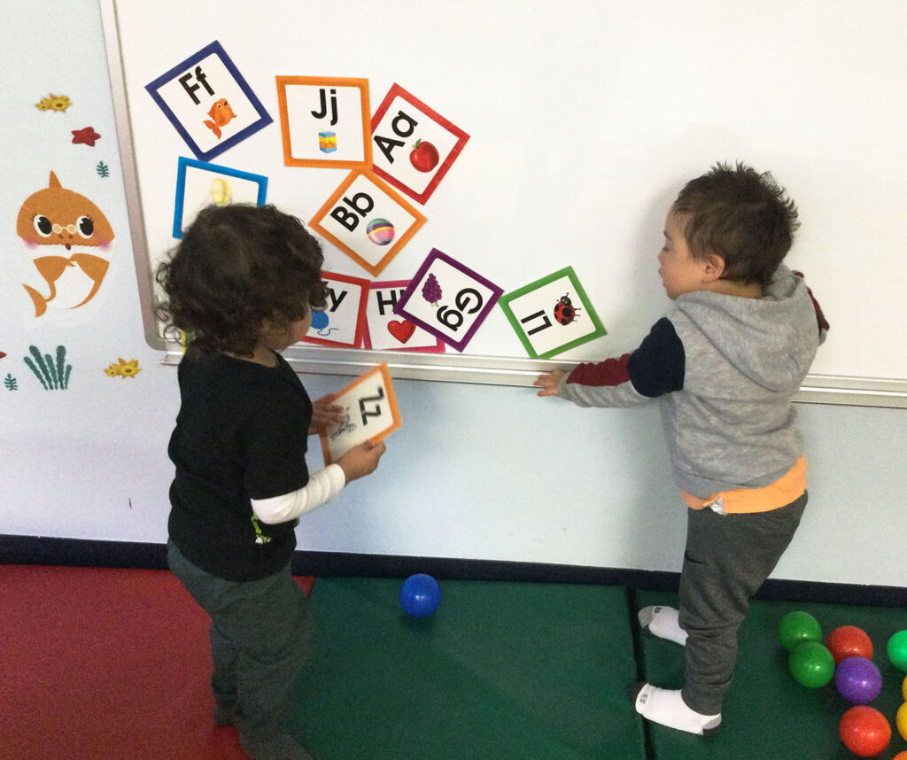 Two male toddlers manipulating alphabet letters on a magnetic board in NJEDDA's Toddler program