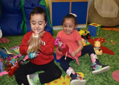 NJEDDA Toddler Program participants playing with dolls and other toys together on the clssroom floor.