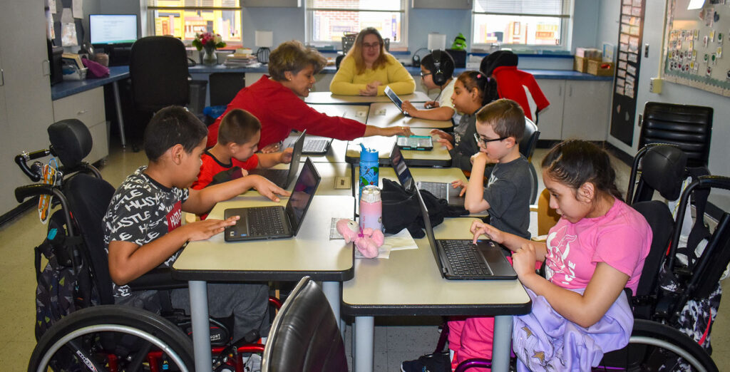 Wide view of an Elementary classsroom at NJEDDA with students working at laptops and tablets
